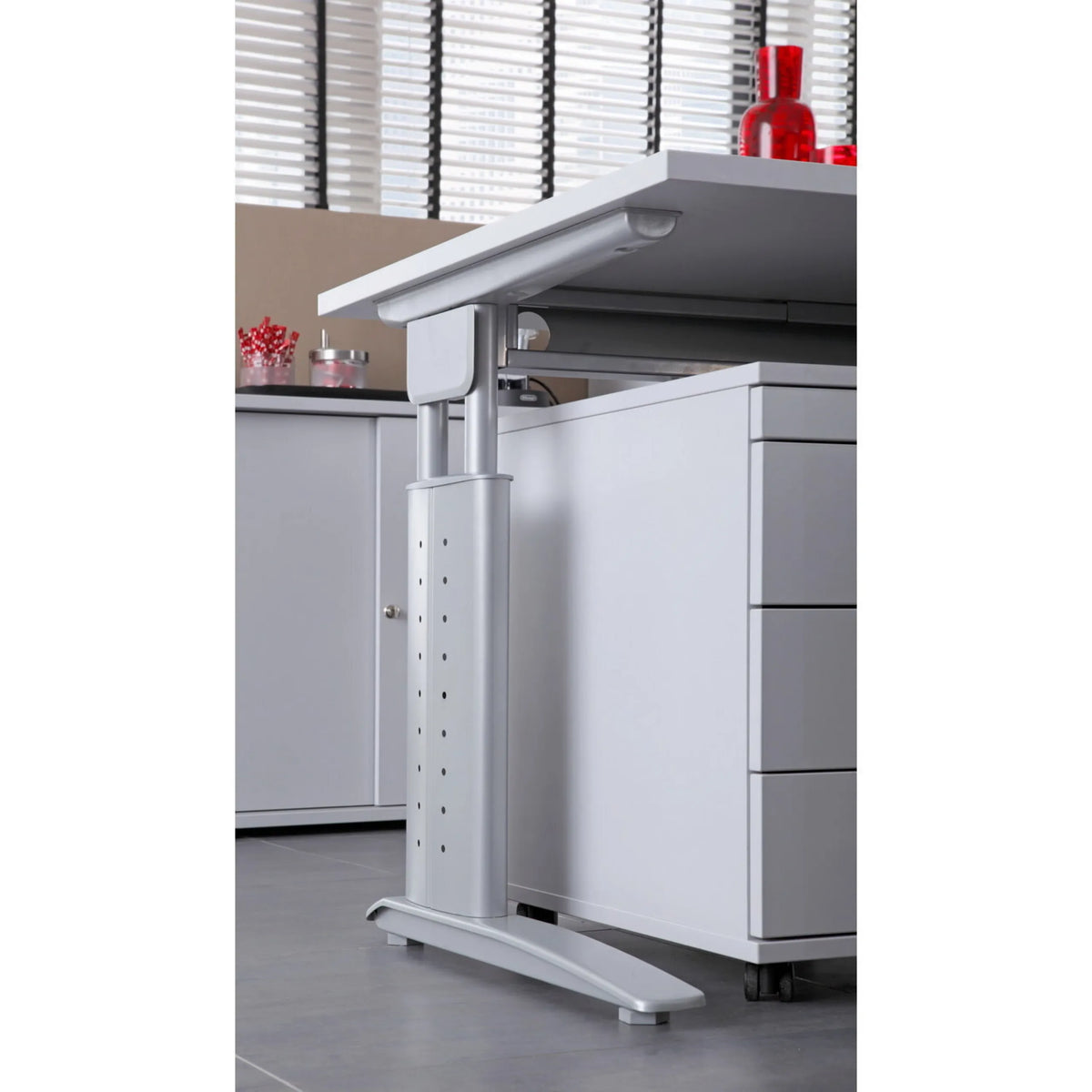 Höhenverstellbares Gestell in Silber des Schreibtischs UNDA 18 S neben einem grauen Rollcontainer von hjh OFFICE PRO